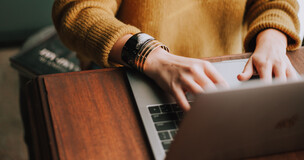 Obrazek przedstawia osobę pracującą przed laptopem.