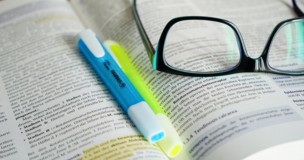 otwarta książka na której leżą okulary oraz dwa zakreślacze