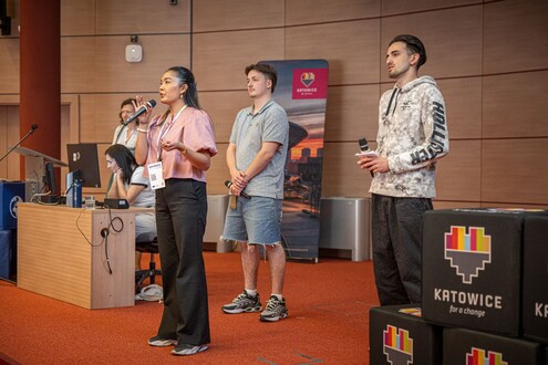 Trzy osoby prezentują coś na scenie w sali wykładowej podczas konferencji technologicznej.