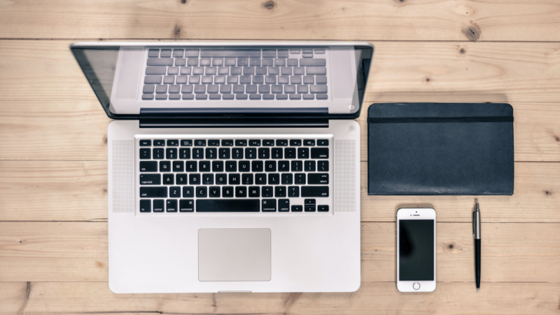 na biurku leży laptop, telefon, tablet i długopis