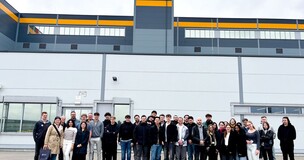 Large group of students posing in front of a logistics center or warehouse during a study visit.
