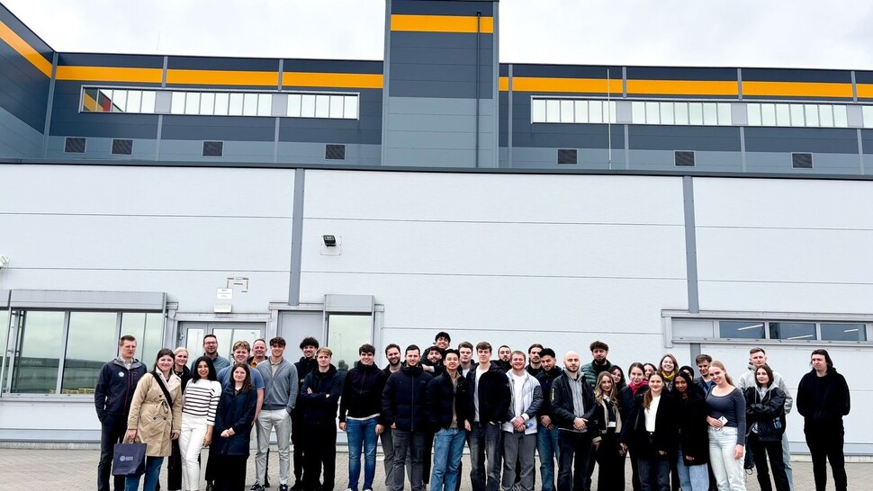 Large group of students posing in front of a logistics center or warehouse during a study visit.