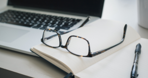 laptop, okulary i notes leżące na biurku