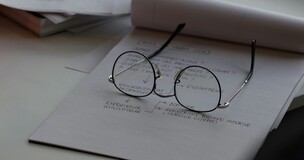 grafika ozdobna, na zdjęciu zapisana kartka papieru i okulary 