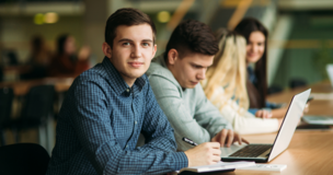 chłopak siedzący ze znajomymi; przed sobą ma laptopa