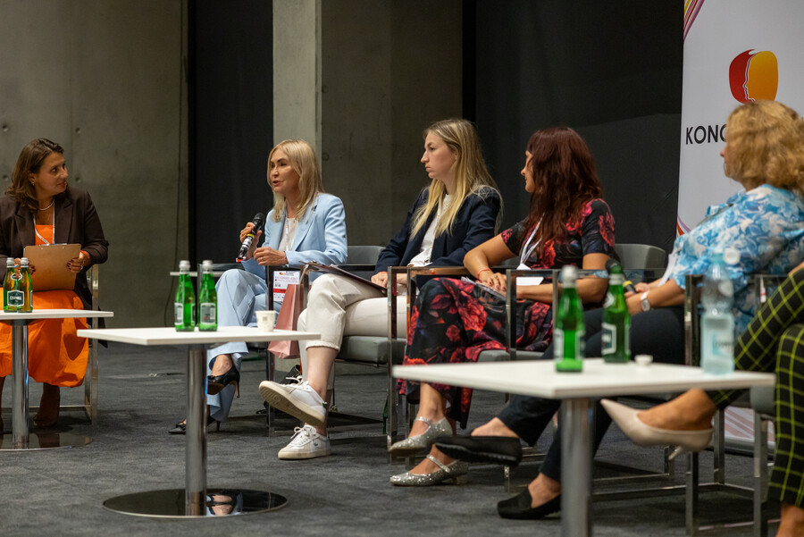 JM Rektor prof. Celina M. Olszak uczestniczy w panelu dyskusyjnym podczas Kongresu Kobiet. Siedzi na fotelu w jasnym garniturze, rozmawia z innymi panelistkami. 