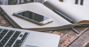 na biurku leży laptop, notes a na notesie telefon