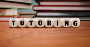 Wooden desk with books and the word “TUTORING” spelled out on letter blocks, promoting student mentoring.