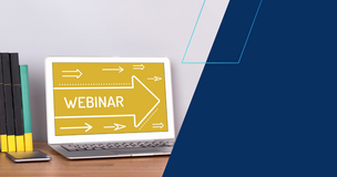 Laptop stojący na drewnianym biurku wyświetla żółty ekran z napisem ‘Webinar’ i białą strzałką skierowaną w prawo; obok znajdują się książki oraz smartfon. Tło po prawej stronie stanowi granatowy blok graficzny.