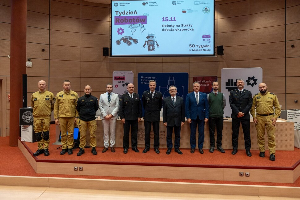 Students and firefighters standing in front of a screen during a robotics-themed science week event.