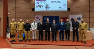 Students and firefighters standing in front of a screen during a robotics-themed science week event.