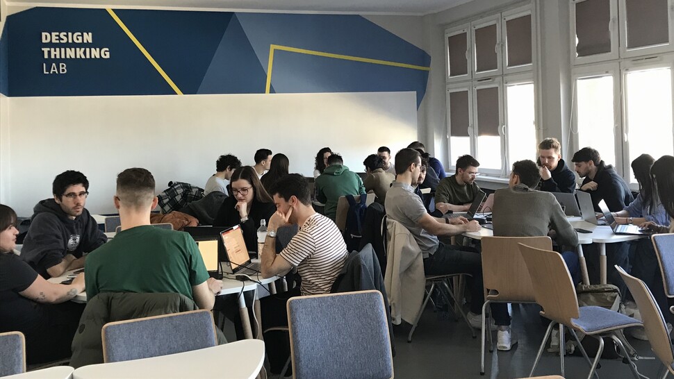 Students seated at tables in a modern classroom, participating in a workshop session for the INTQUANT project.