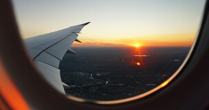 Airplane wing seen through the window during flight, symbolizing international student travel opportunities.