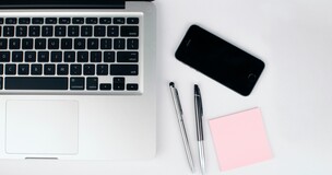 na biurku leży laptop, karteczki do notowania i telefon