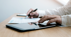 tablet, w tle kartka papieru, przy stole mężczyzna, który patrzy na rzeczy