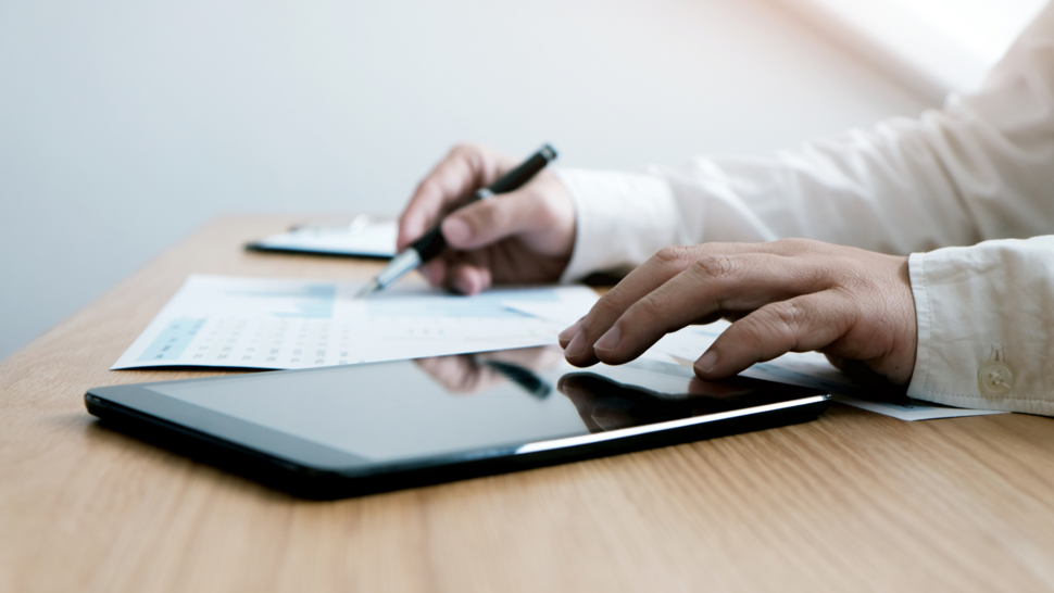tablet, w tle kartka papieru, przy stole mężczyzna, który patrzy na rzeczy