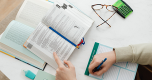 dłonie trzymające długopis, w tle otwarte książki