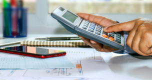 męska dłoń używająca kalkulatora, dokumenty, telefon w tle