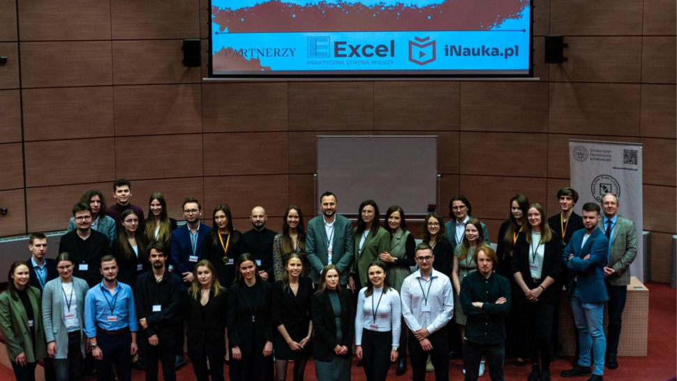 Na środku sali stoi grupa uczestników konkursu, za nią jest umieszczony rzutnik