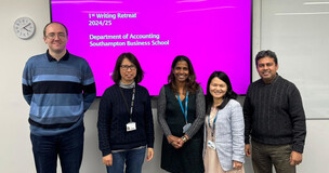 Five academic staff members posing for a group photo in front of a pink presentation screen.