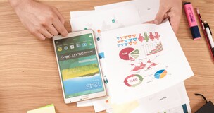 Person working at a desk with charts and a smartphone, representing academic publication in international databases.