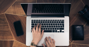 Na biurku leży laptop, telefon, portfel i fotograf