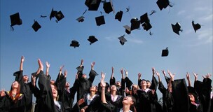 Młodzi ludzie w strojach absolwentów podrzucają czapki w górę. Cieszą się z ukończenia studiów.