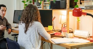 dwie osoby siedzące przy biurku i prowadzące rozmowę