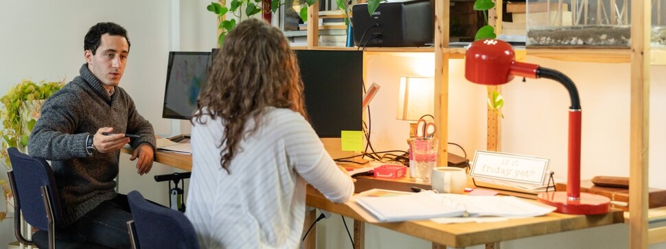dwie osoby siedzące przy biurku i prowadzące rozmowę