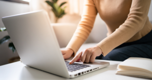 damska postać siedząca przed laptopem, obok notatnik