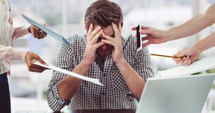 Młody mężczyzna siedzący przed laptopem. Trzyma się za głowę i jest wyraźnie zestresowany.