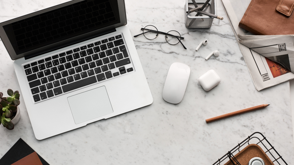 na biurku leży laptop, telefon, słuchawki, okulary, ołówek oraz kwiatek w doniczce