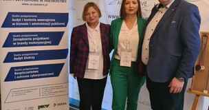 uczestnicy wydarzenia stojący przy banerze reklamującym studia podyplomowe