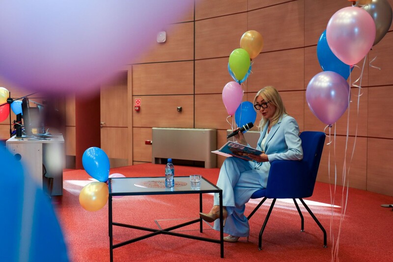 JM Rektor prof. Olszak czytająca bajkę dzieciom; w tle kolorowe balony