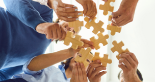 osoby trzymające duże, drewniane puzzle