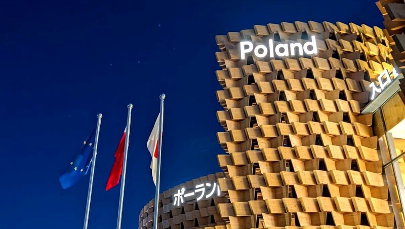 Nowoczesny budynek w Osace z napisem Poland, po lewej 3 flagi: Europejska, Polska i Japońska