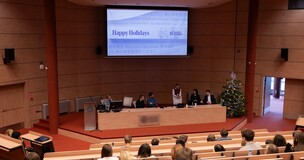 spotkanie z tyłu auli; w tle prelegenci oraz slajd z prezentacji z napisem "happy holidays" 