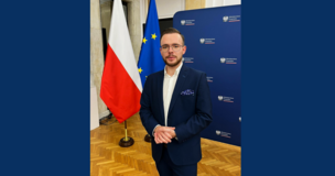 Student standing and smiling in front of a Polish flag and Ministry of Finance banner.