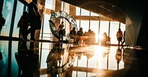 Participants seated in a circular hall with a lit university emblem in the background during the PRIME-UNIBAGUÉ lecture series.