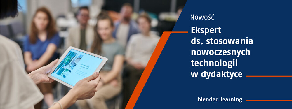 Zbliżenie na tablet trzymany przez osobę prowadzącą zajęcia, w tle studenci.