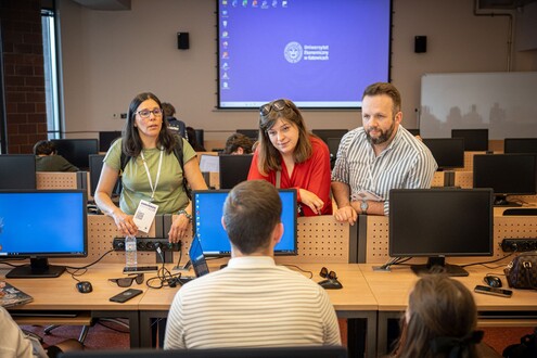 Grupa uczestników siedzi przy komputerach podczas warsztatów lub prezentacji w sali konferencyjnej.