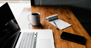laptop, notes i kubek leżące na biurku