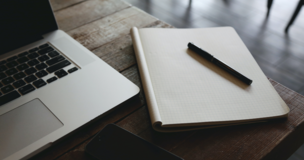 na biurku znajduje się laptop, notes oraz długopis