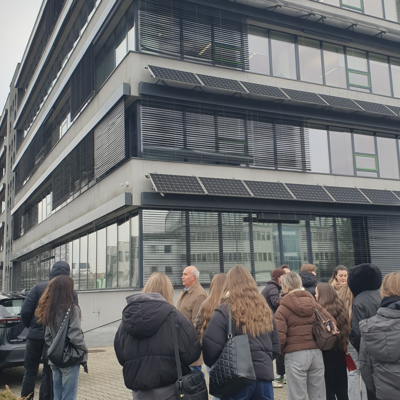 Studenci przed budynkiem z panelami słonecznymi na elewacji.