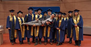 Group of graduates in academic gowns and caps posing for a photo during the MBA graduation ceremony.