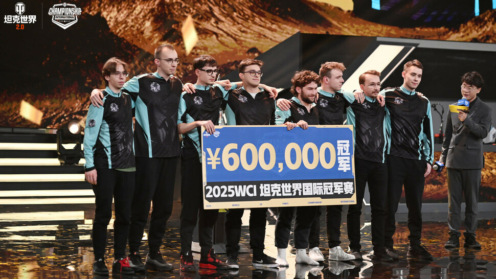 Grupa ośmiu zawodników drużyny e-sportowej stoi na scenie turniejowej, trzymając dużą tablicę z napisem ‘¥600 000’ i ‘2025 WCI’. Wszyscy ubrani są w czarno-turkusowe stroje drużynowe. Obok nich stoi prowadzący z mikrofonem. W tle widoczne są elementy scenografii w złoto-czarnych barwach.