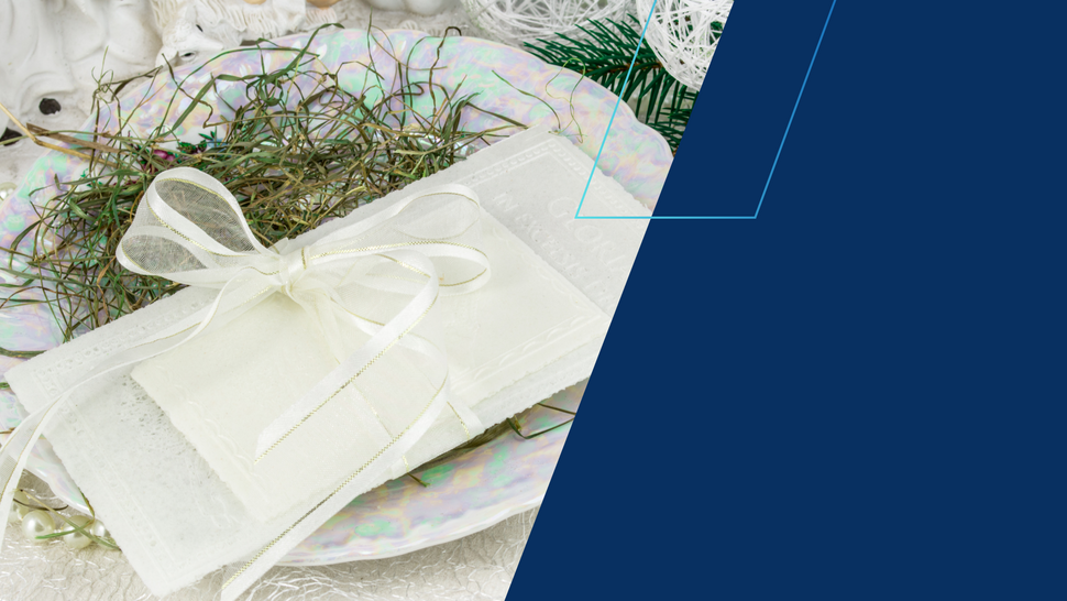 Biały opłatek przewiązany ozdobną, kremową wstążką leży na talerzu udekorowanym siankiem świątecznym; w tle białe, bożonarodzeniowe ozdoby i gałązki świerku. Po prawej stronie znajduje się duże, granatowe pole graficzne.