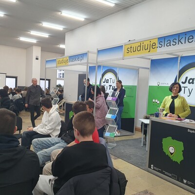 Uczniowie szkół wysłuchujący wykładu oraz dr Beata Dubiel przy stoisku.