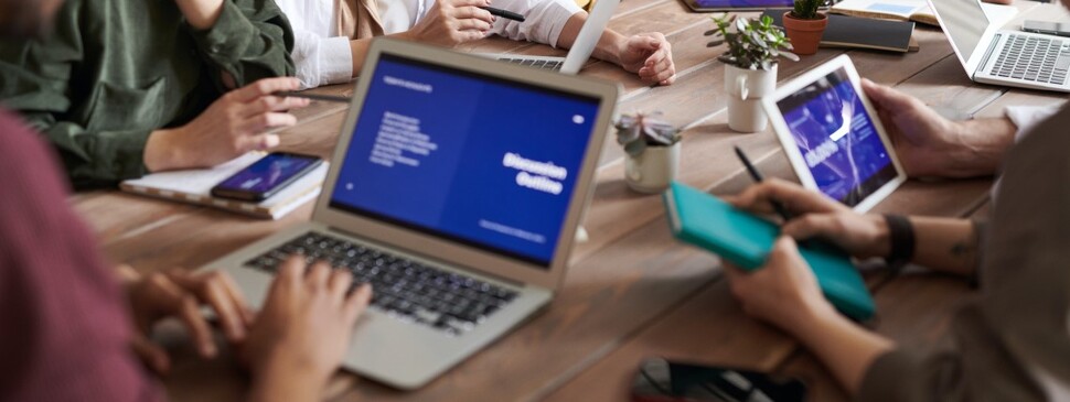 grupa ekspertów zgromadzona przy stole konferencyjnym z laptopami, tabletami i smartfonami