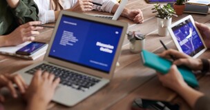 grupa ekspertów zgromadzona przy stole konferencyjnym z laptopami, tabletami i smartfonami